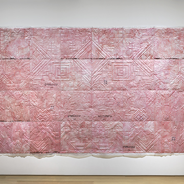 a large, pink wall hanging consisting of squares stitched with geometric lines